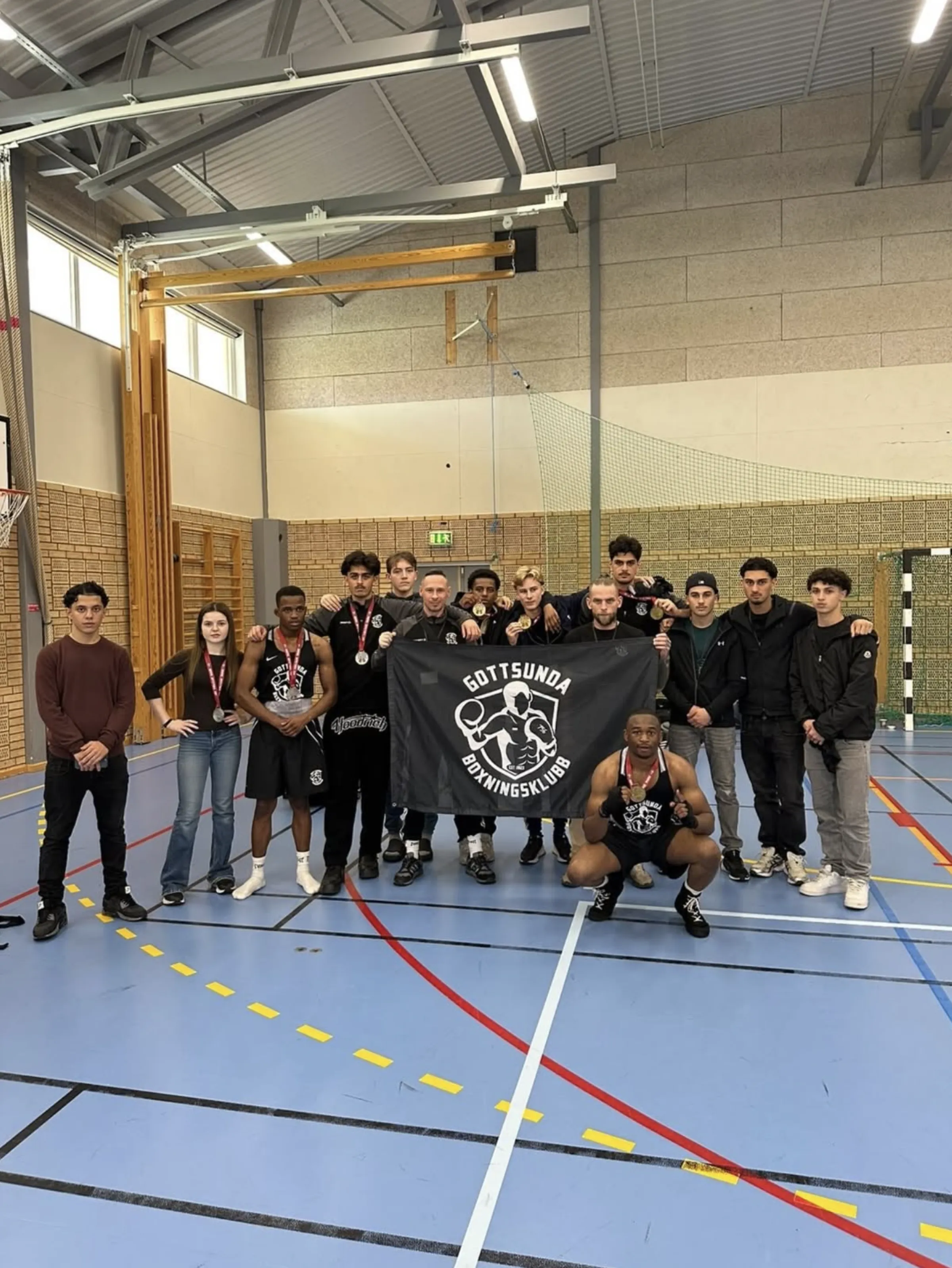 Klubbmedlemmar poserar med klubbens banderoll i en idrottshall